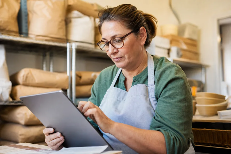 Small business owner in a bakery back office looking at a website on a tablet