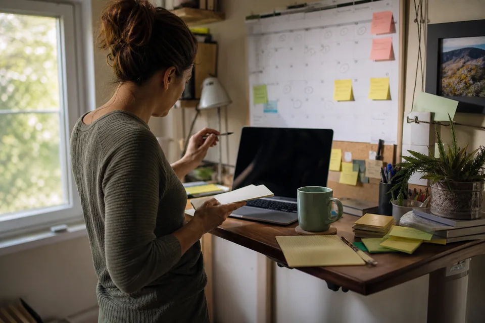 Domain investor at a standing desk checking a laptop calendar of names about to drop, coffee and notebook beside her