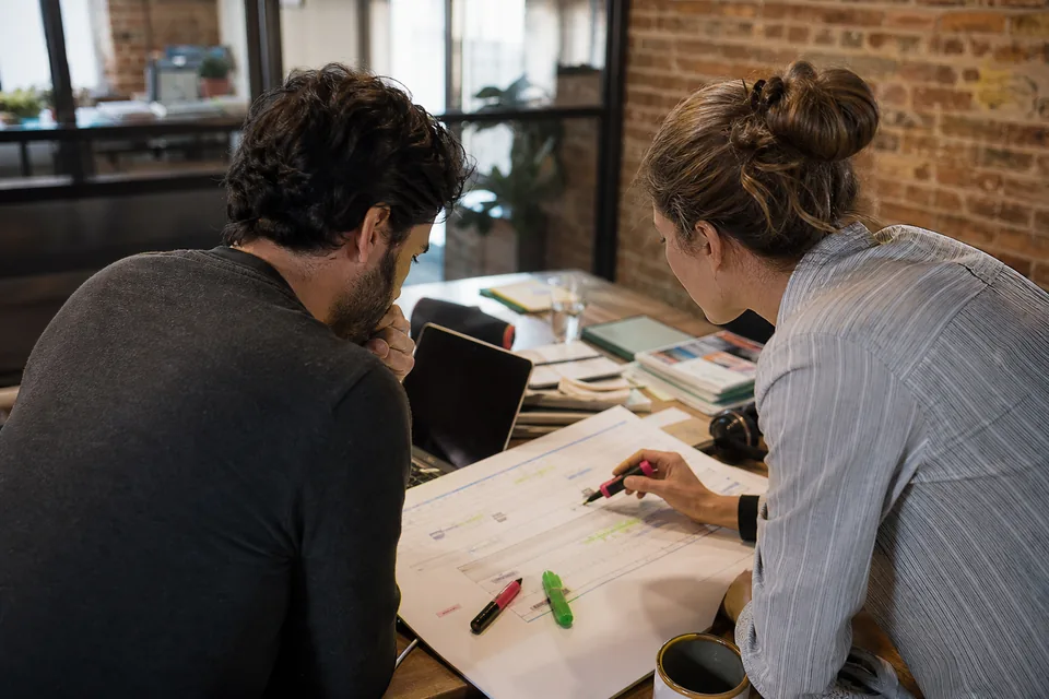 Agency founder and colleague comparing a printed timeline of expiring names at a workshop table