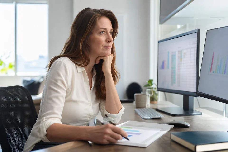 Domain investor at a two-monitor desk comparing a shortlist of expired domains against charts